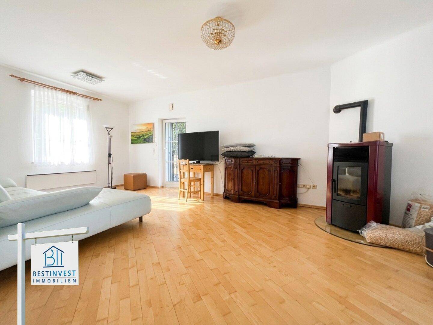 Geräumiges Wohnzimmer mit hellem Sofa, Holzofen und Holzdielenboden.