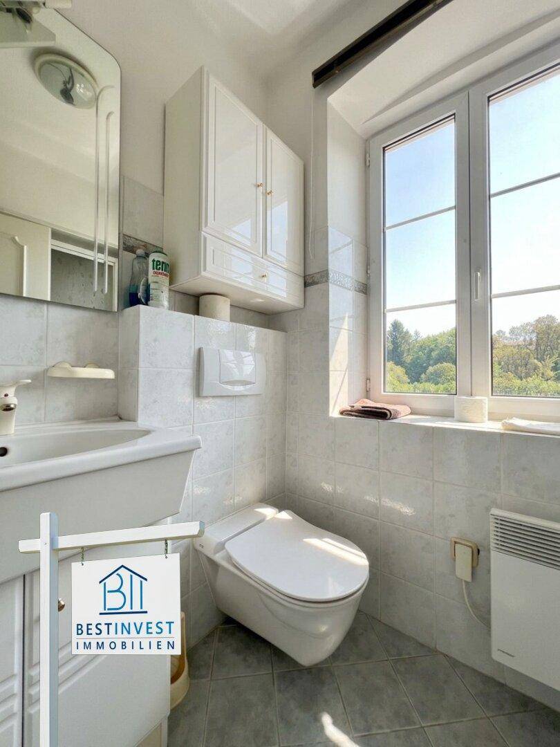 Kleines WC mit Toilette, Waschbecken, Fenster und hellen Fliesen.