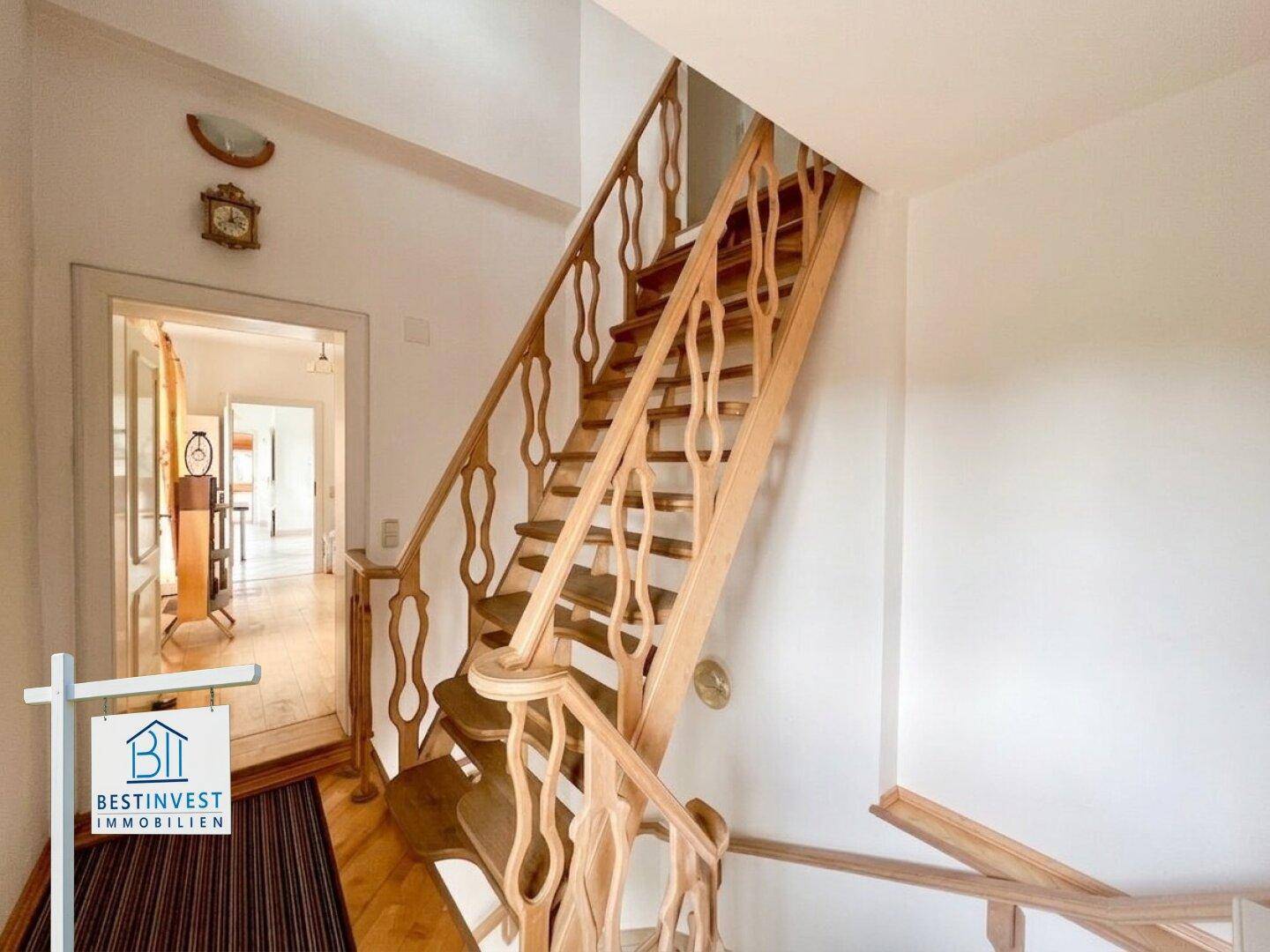 Helles Treppenhaus mit einer eleganten Holztreppe und weiß gestrichenen Wänden.