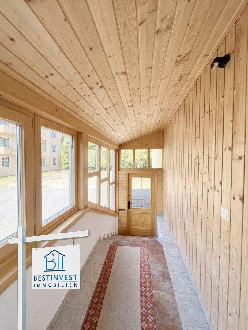 Heller Wintergarten mit Holzverkleidung an Wänden und Decke sowie großen Fenstern.