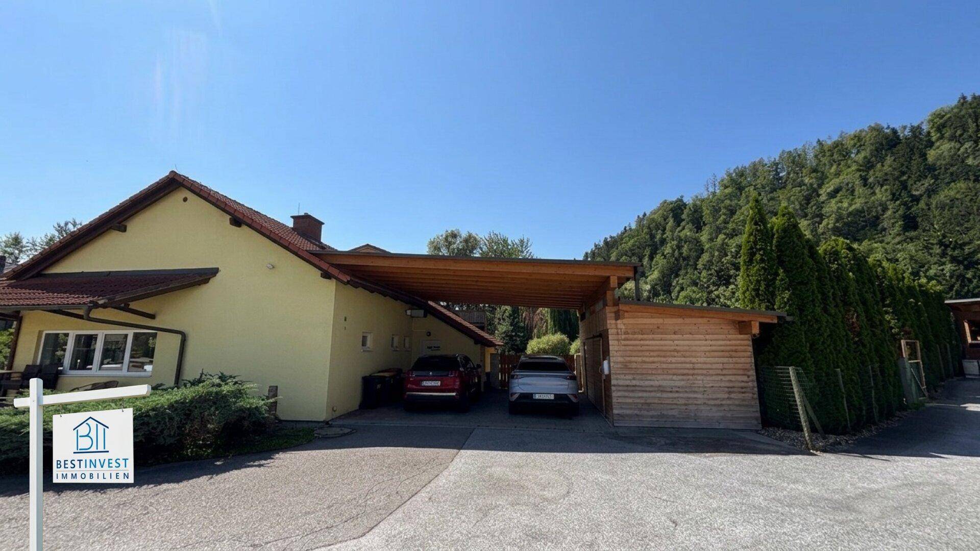 Geräumiger Carport mit zwei Stellplätzen und angrenzendem Holzschuppen im Grünen.
