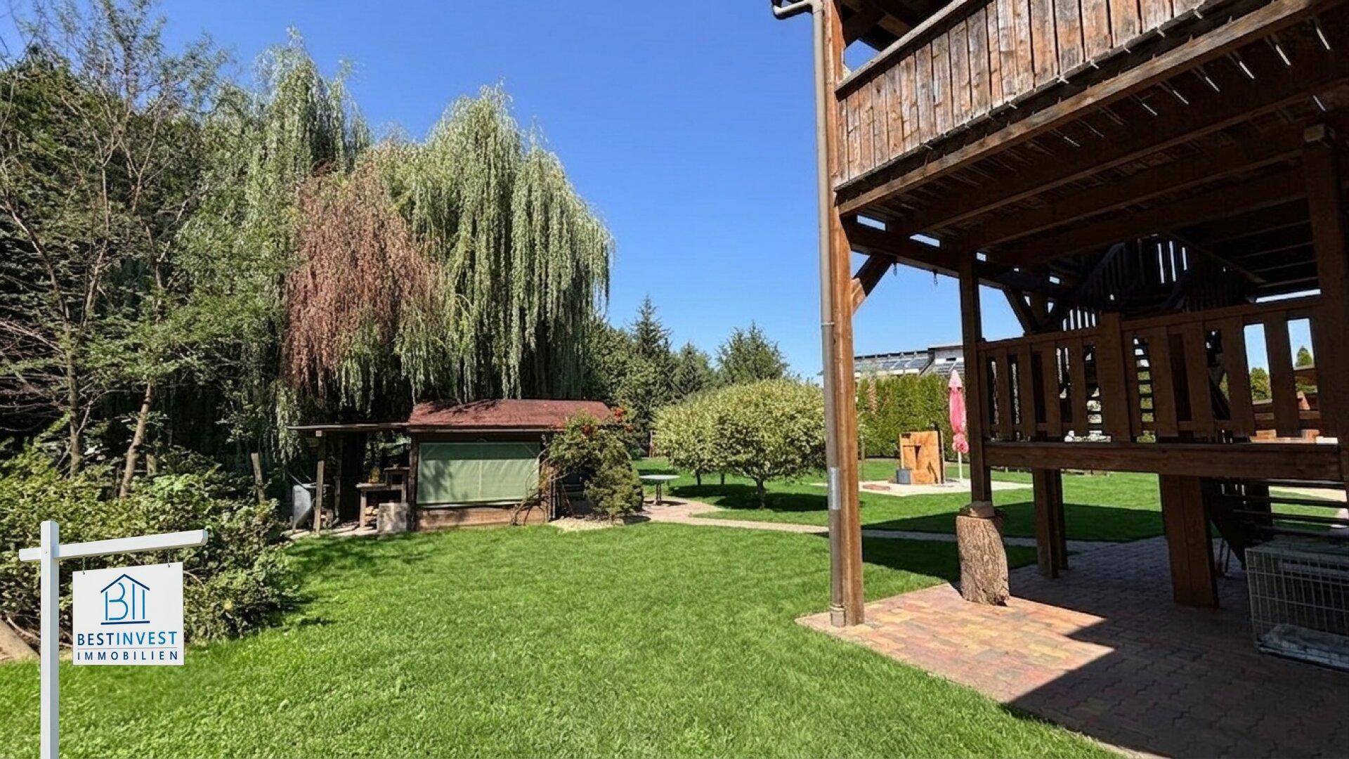 Gepflegter Garten mit Rasen, einem kleinen Holzhaus und einem erhöhten Holzbalkon.
