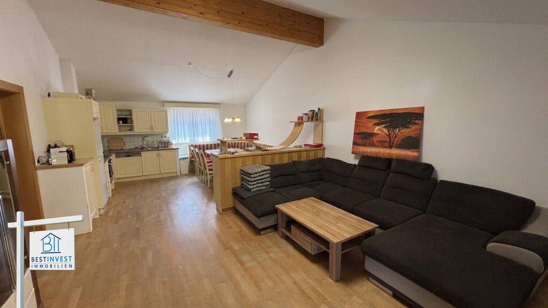 Offener Wohnbereich mit integrierter Küche, Holzboden und sichtbaren Deckenbalken.