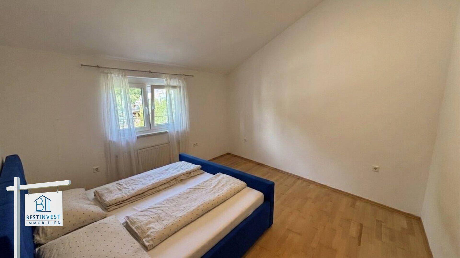 Helles Schlafzimmer mit Holzboden, Fenster und schräger Decke.