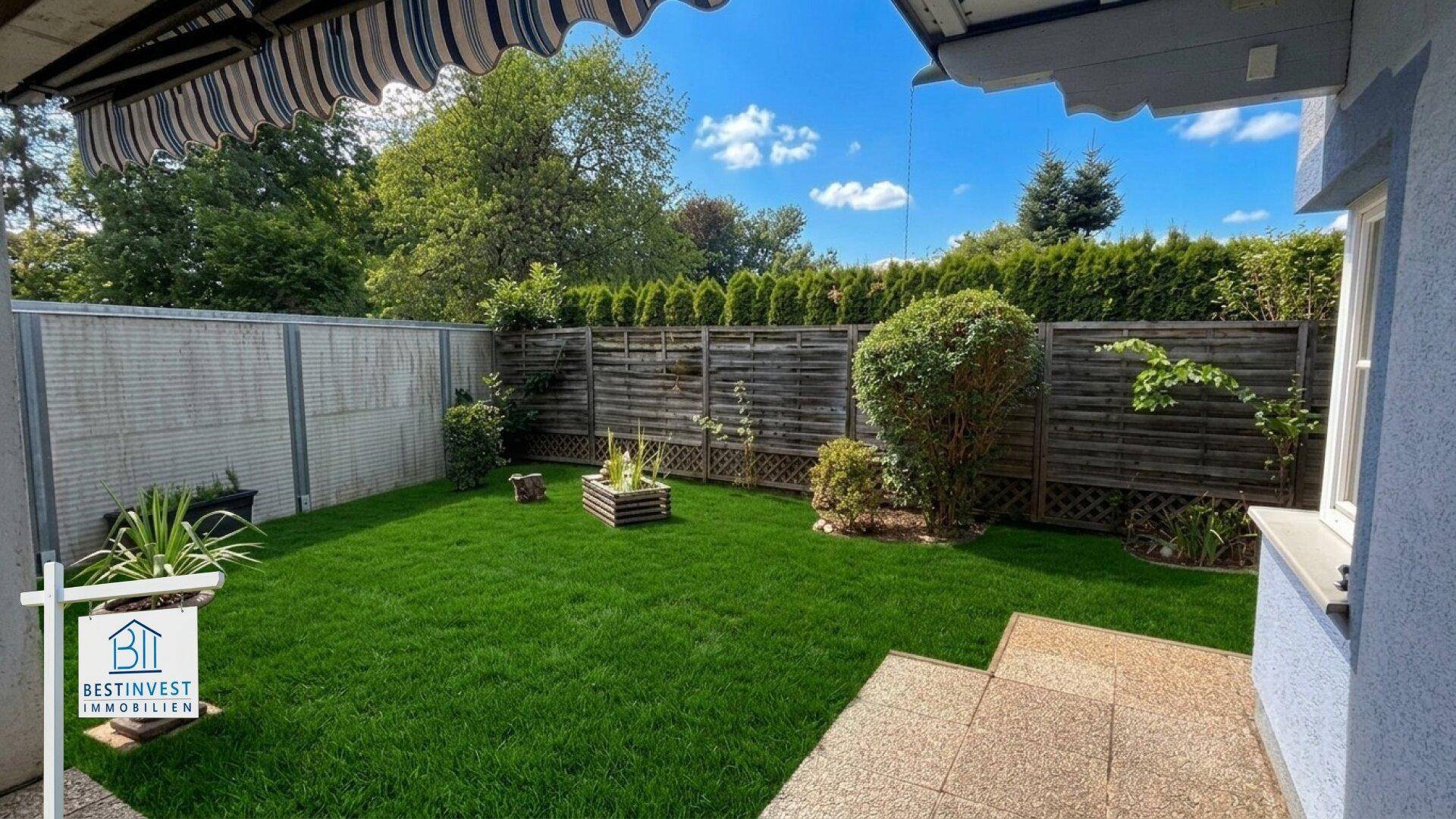 Gepflegter Gartenbereich mit Rasenfläche und hoher Hecke als Sichtschutz.