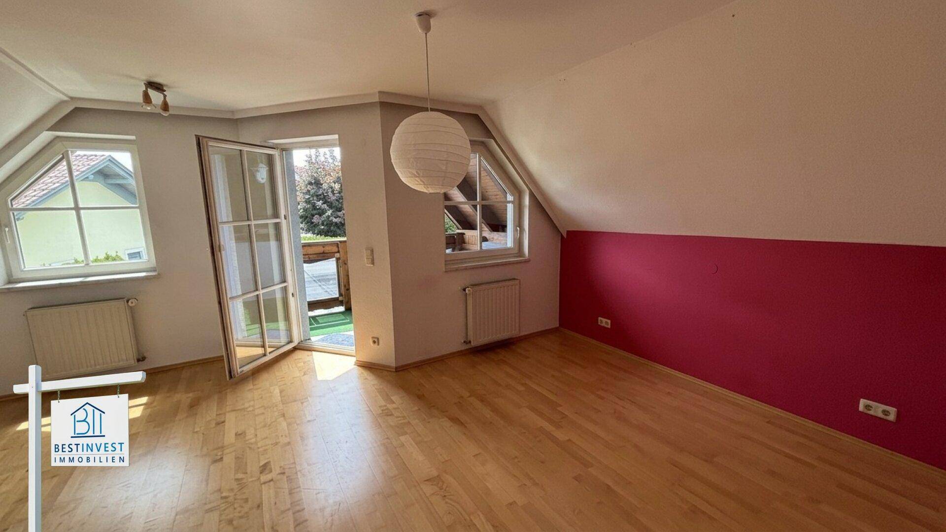 Helles Dachgeschosszimmer mit Holzboden, roter Akzentwand und Balkonzugang.