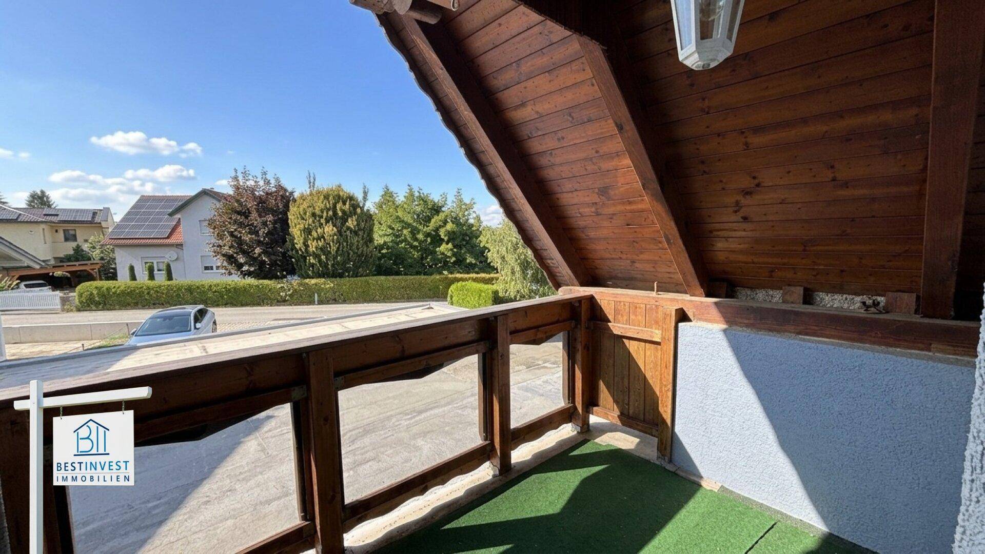Kleiner Balkon mit Holzboden und Blick auf die Straße und Bäume.