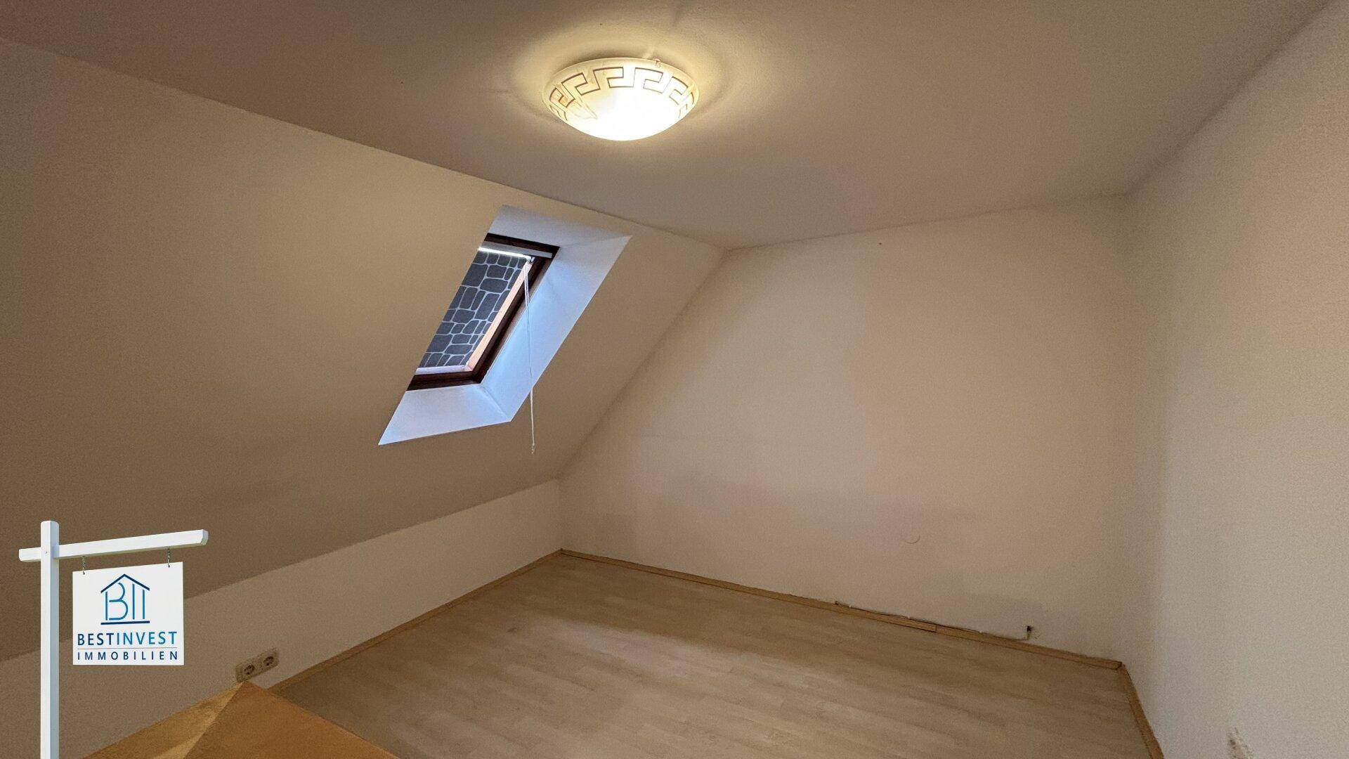 Leeres Dachgeschosszimmer mit Dachfenster und schrägen Wänden.