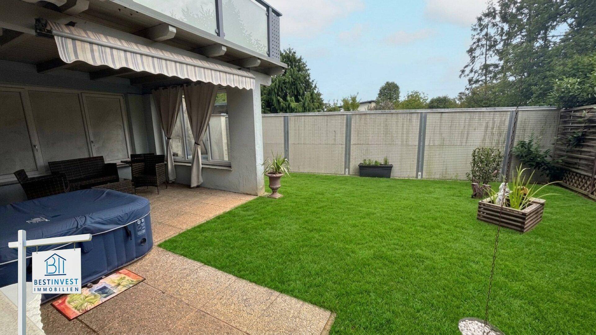 Große Terrasse mit Whirlpool und Rasenfläche, umgeben von einem Zaun für Privatsphäre.