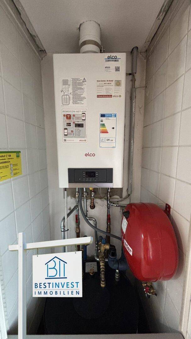 Heizungsraum mit moderner Gastherme und Warmwasserspeicher, umgeben von Fliesen.