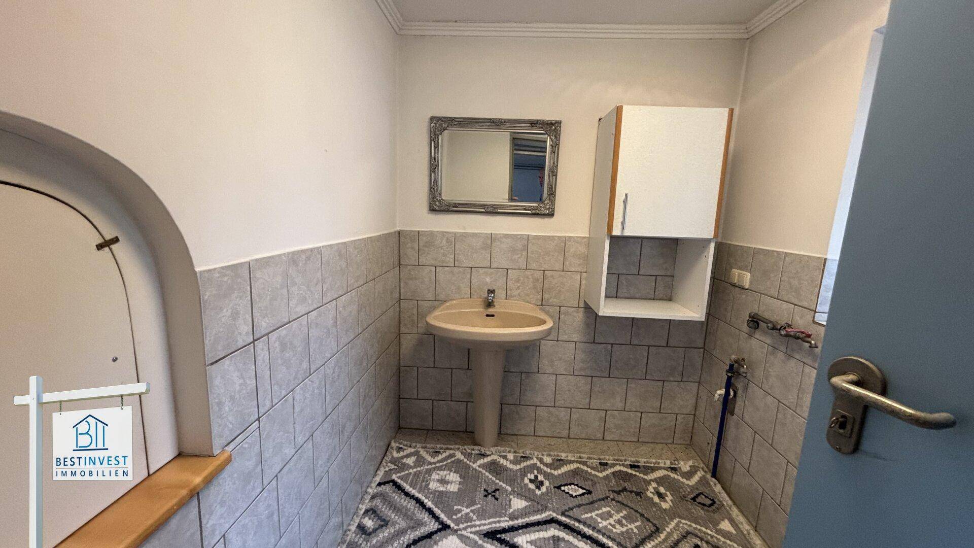 Kleines Gäste-WC mit Waschbecken, Spiegel und halbhohen Fliesen an den Wänden.