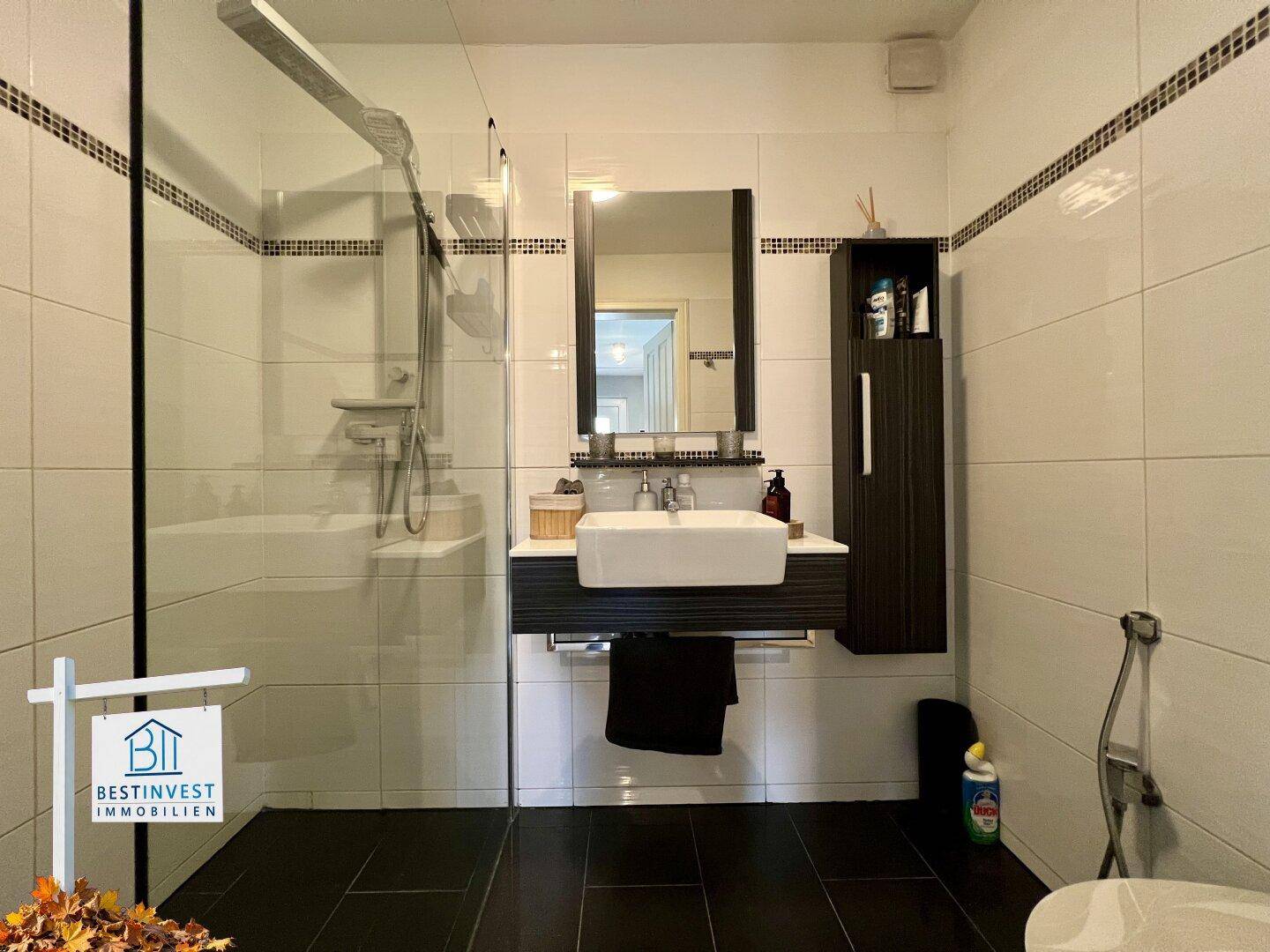 Modernes Badezimmer mit ebenerdiger Dusche, stilvollem Waschbecken und dunklen Bodenfliesen.