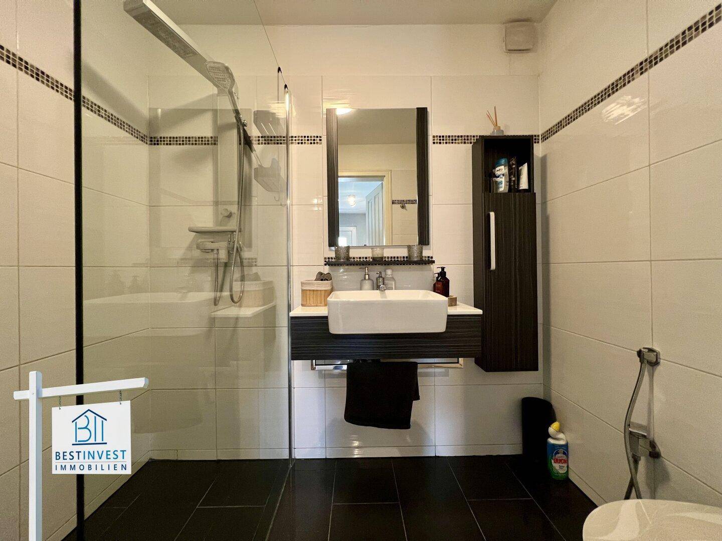 Modernes Badezimmer mit ebenerdiger Dusche, dunklen Fliesen und stilvollem Waschbecken.