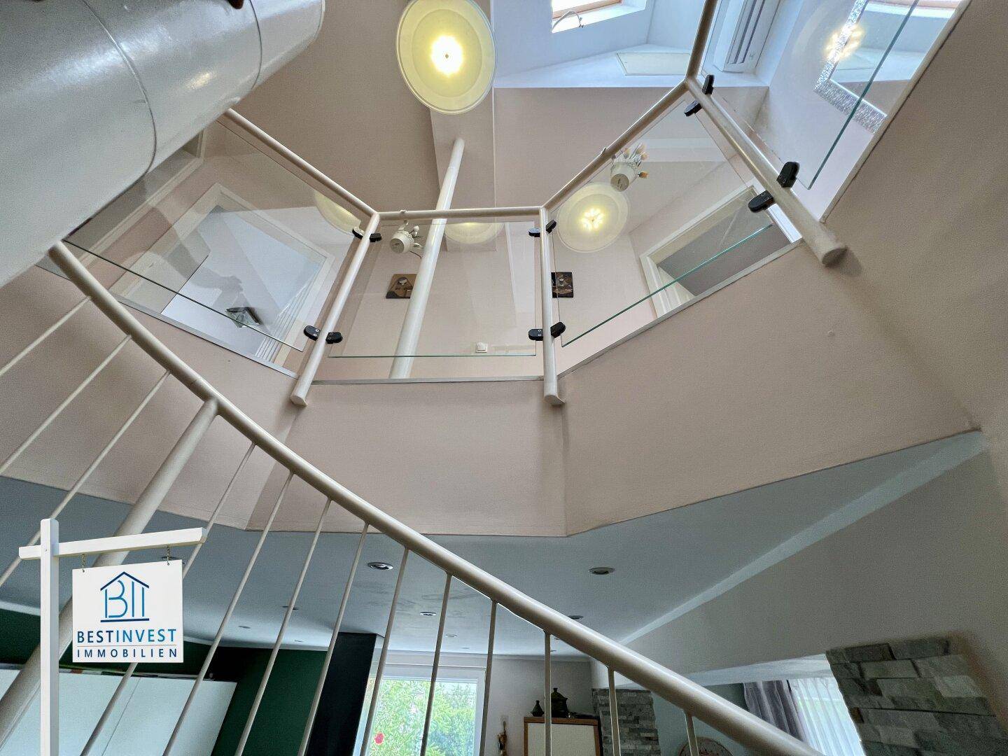 Blick von oben auf die Wendeltreppe mit Glasgeländer und heller Deckenbeleuchtung.