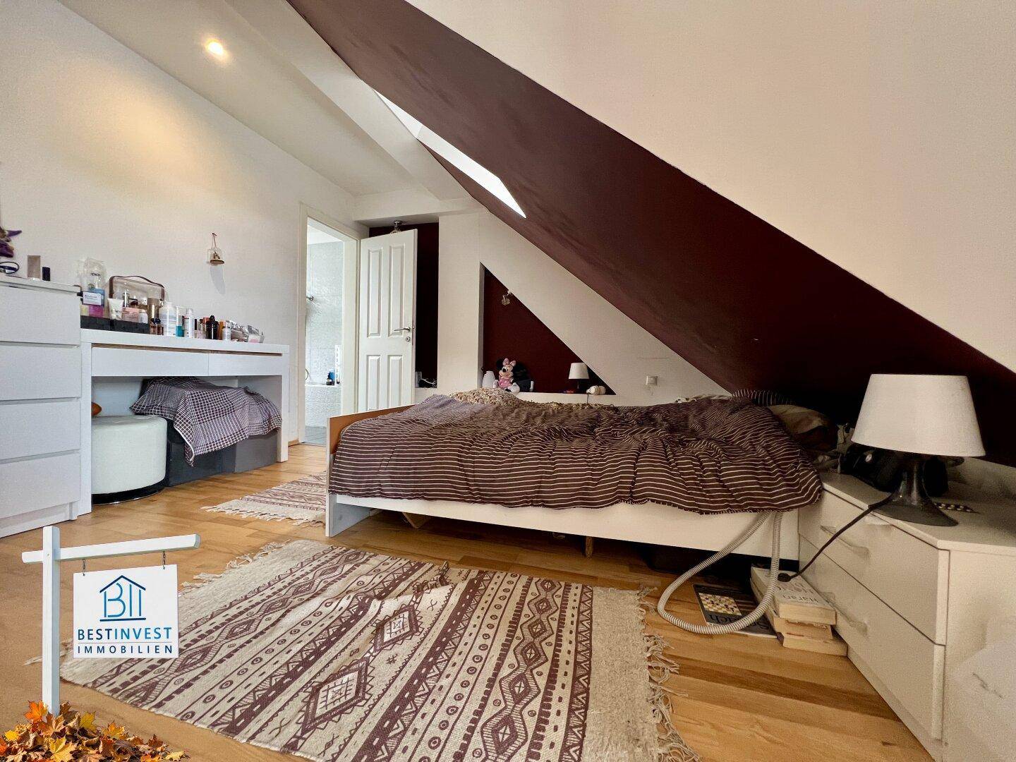 Helles Schlafzimmer mit Holzboden, Dachschräge und praktischem Arbeitsbereich.