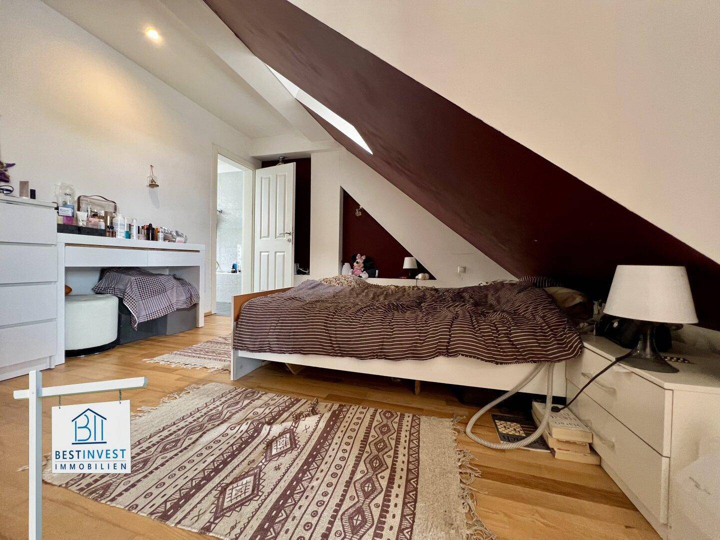 Helles Schlafzimmer mit Holzboden, Dachschräge und Blick auf den Balkon.