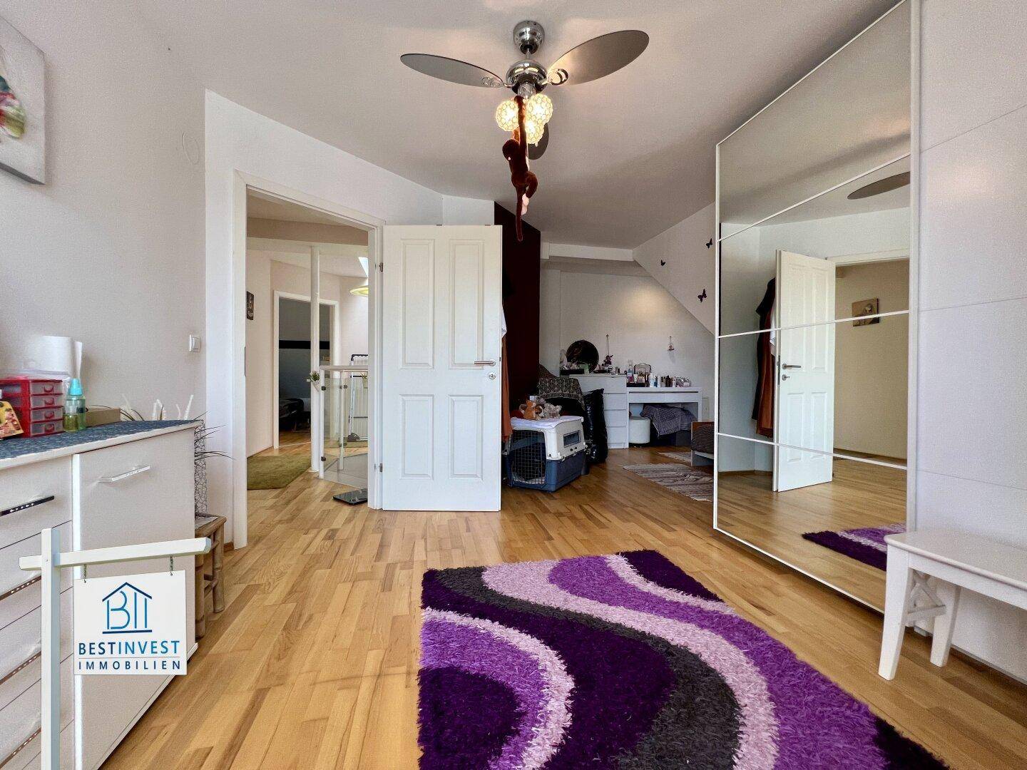 Helles Schlafzimmer mit Holzboden, Spiegelschrank und Deckenventilator.