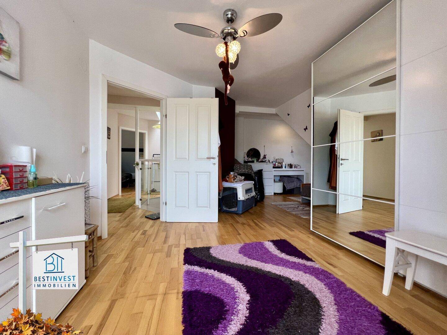 Schlafzimmer mit Holzboden, Spiegelschrank und Deckenventilator, hell und funktional.