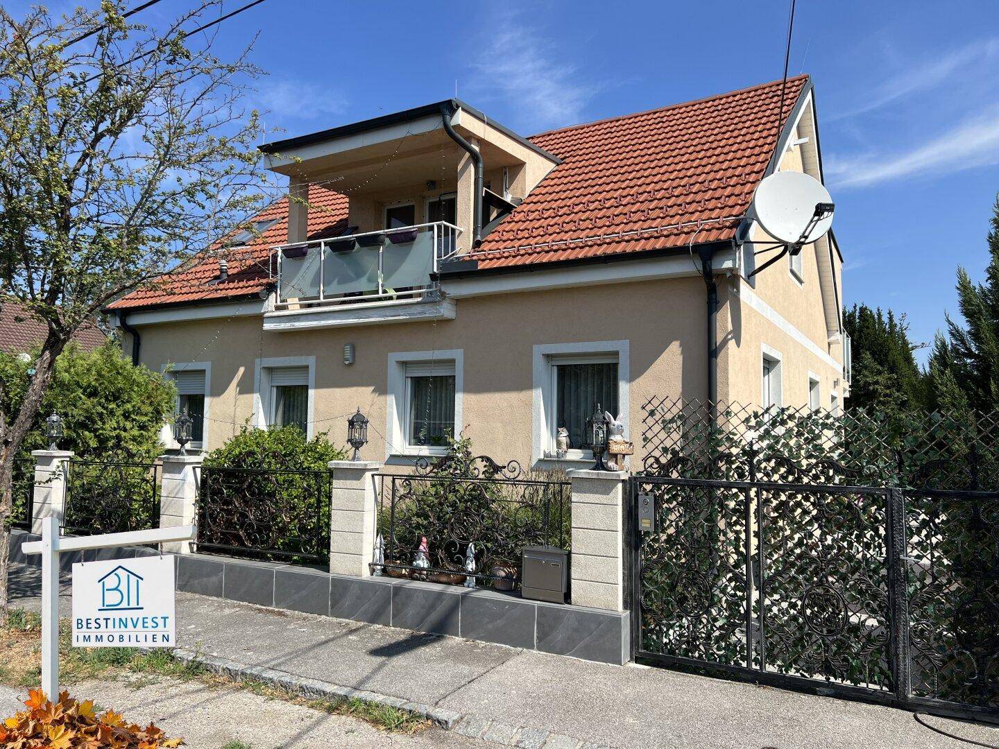 Vorderansicht des Hauses mit rotem Ziegeldach, Balkon und einem dekorativen schmiedeeisernen Zaun.