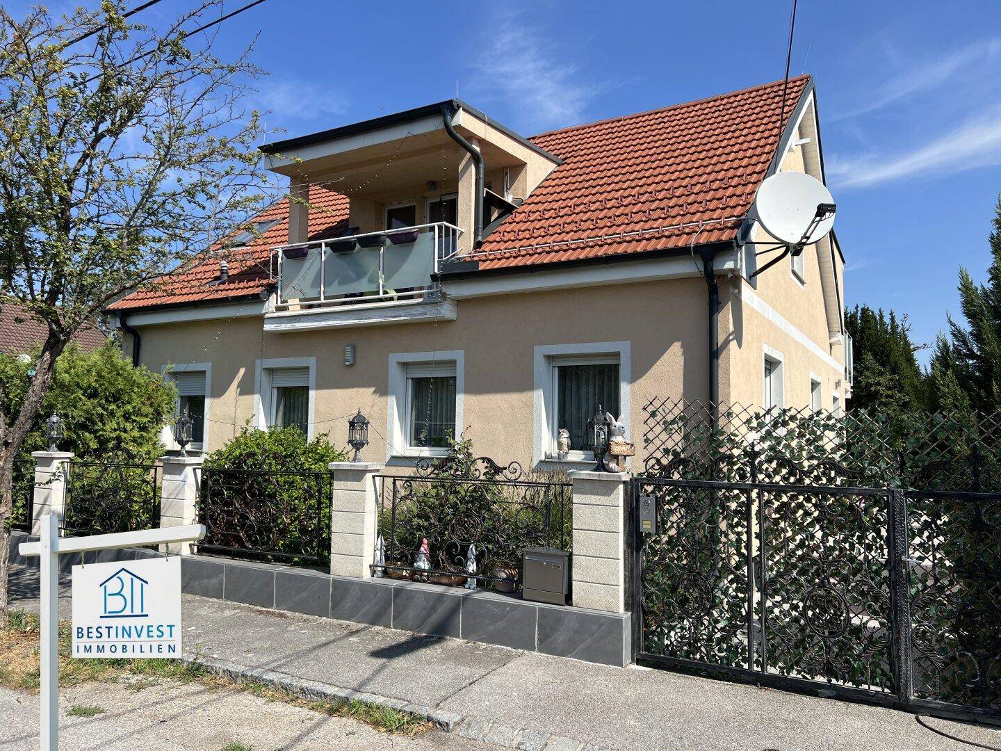 Vorderansicht des Hauses mit rotem Ziegeldach, Balkon und schmiedeeisernem Zaun.