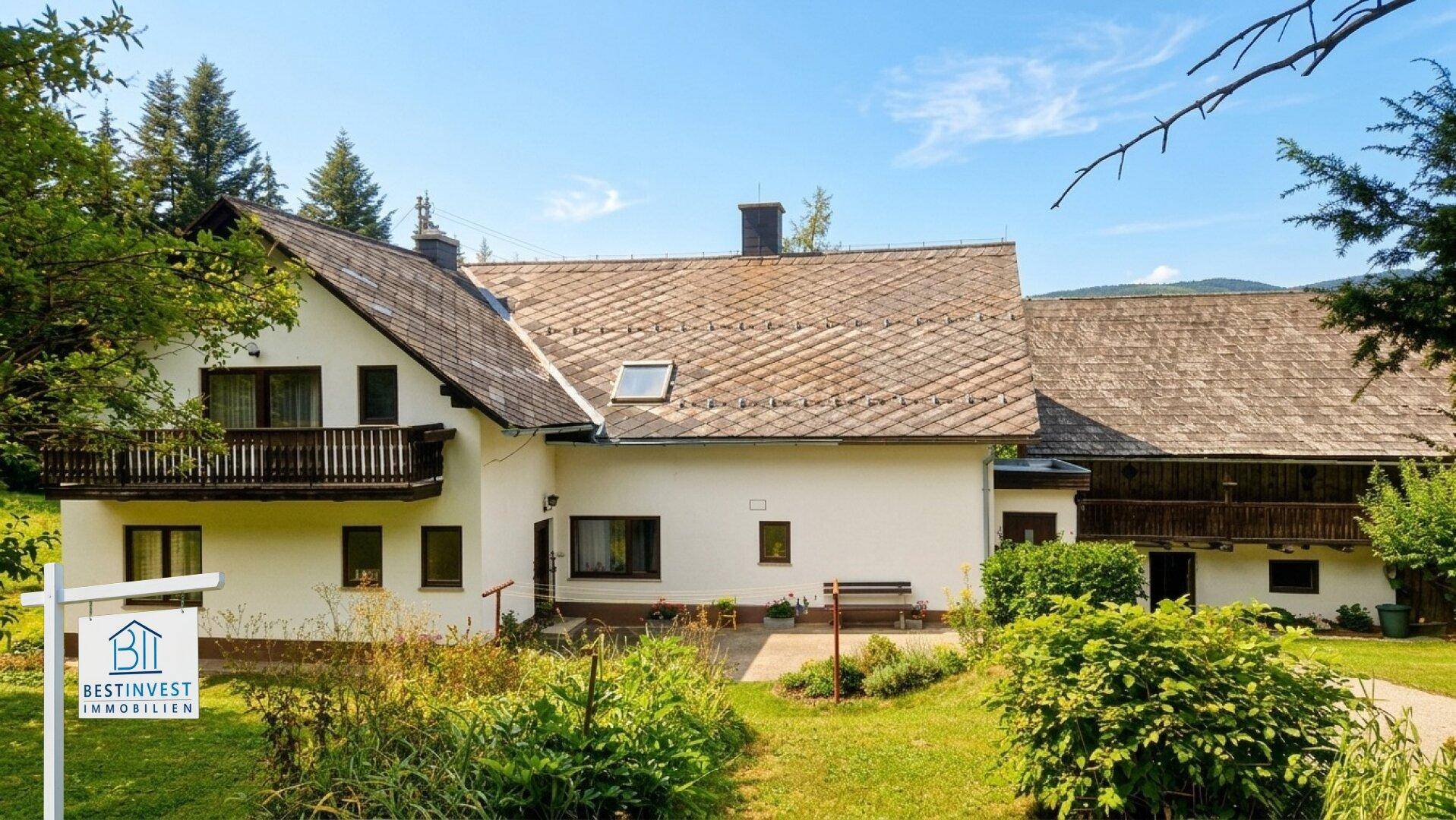 Traditionelles Landhaus mit Holzbalkon und Satteldach, umgeben von grüner Natur.