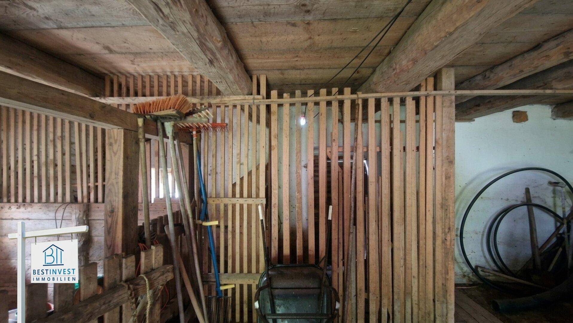 Innenansicht der Scheune mit Holzabtrennungen und landwirtschaftlichen Geräten.