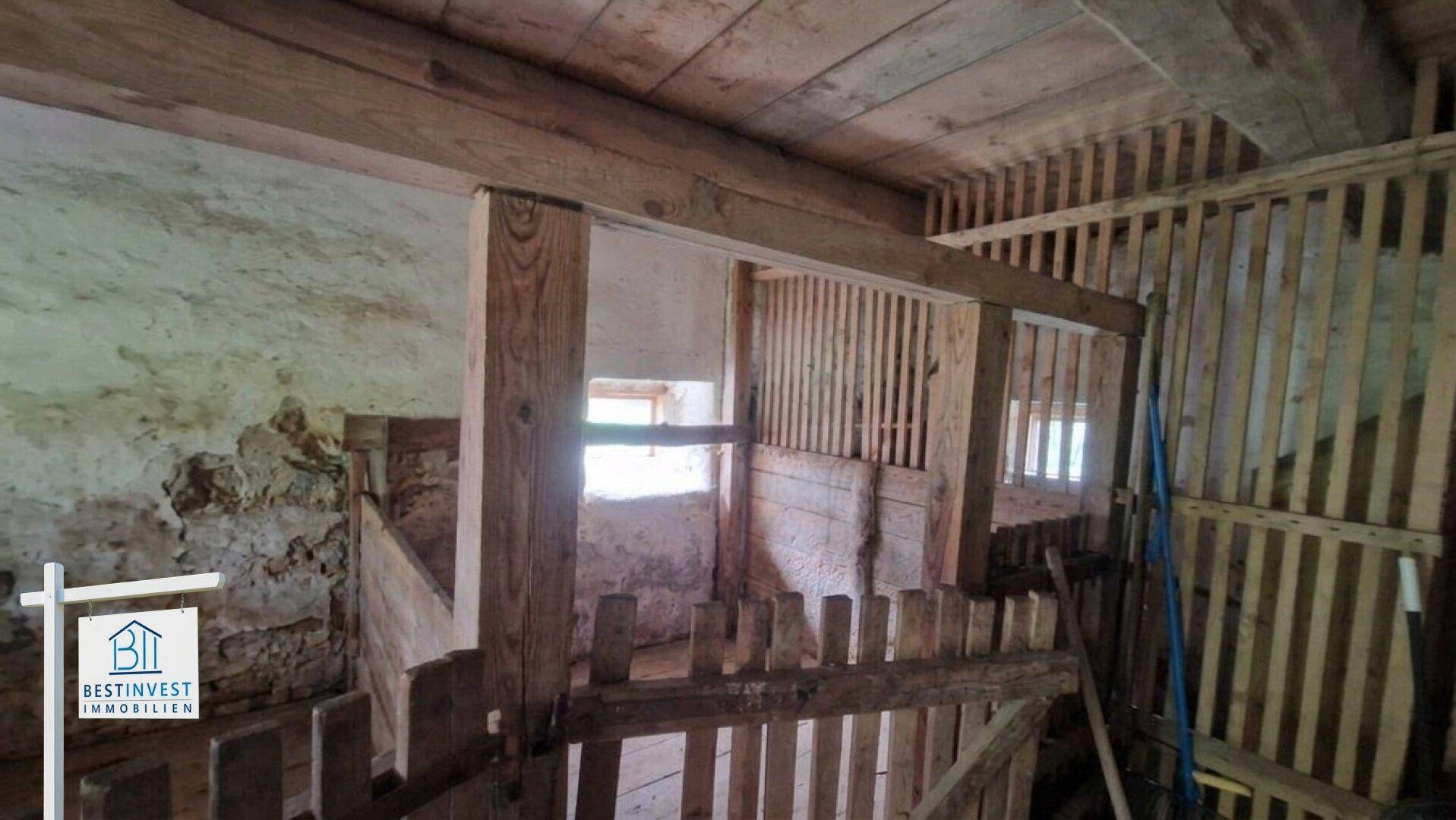 Rustikale Tierställe im Inneren der Scheune mit Holzbalken und Steinwänden.