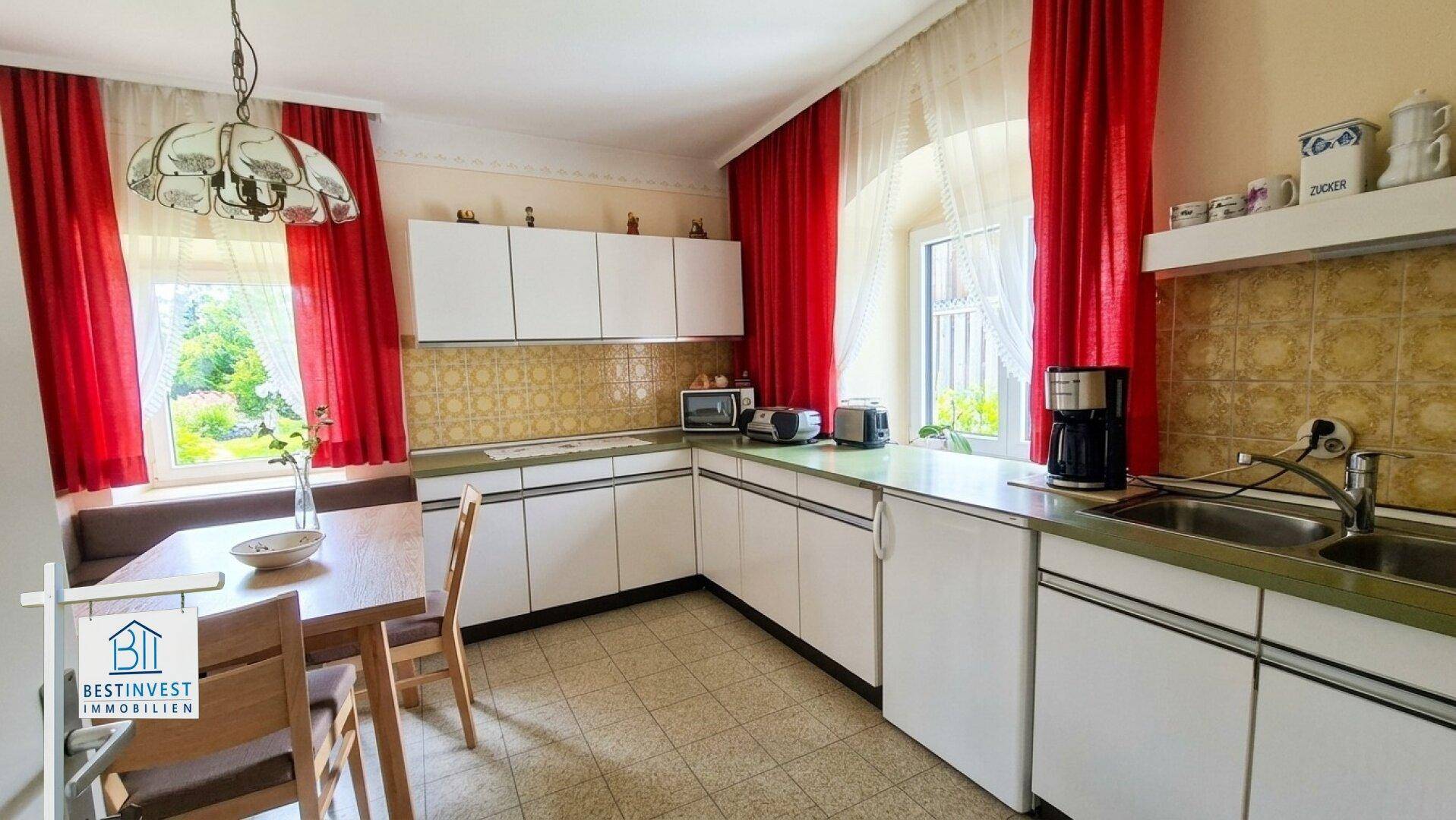 Helle Küche mit Essbereich, weißen Schränken und Blick in den Garten.