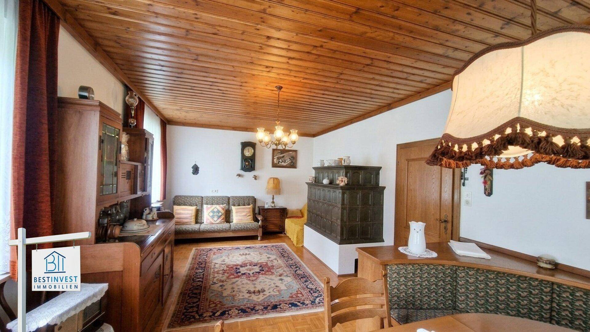Gemütliches Wohnzimmer im alpinen Stil mit Holzbalkendecke und traditionellem Kachelofen.