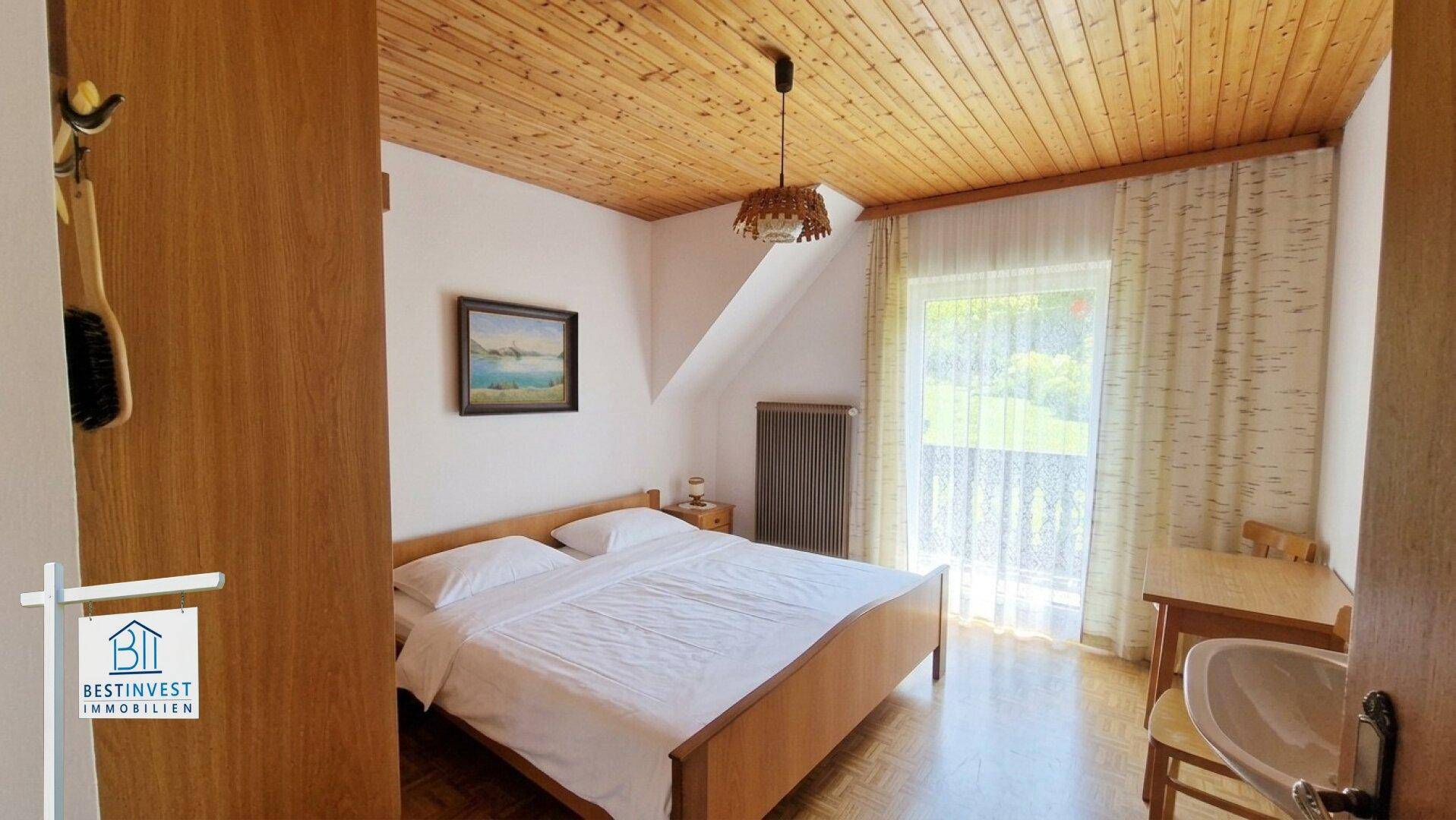Schlafzimmer mit Holzbalkendecke, Doppelbett und Zugang zum Balkon mit Bergblick.