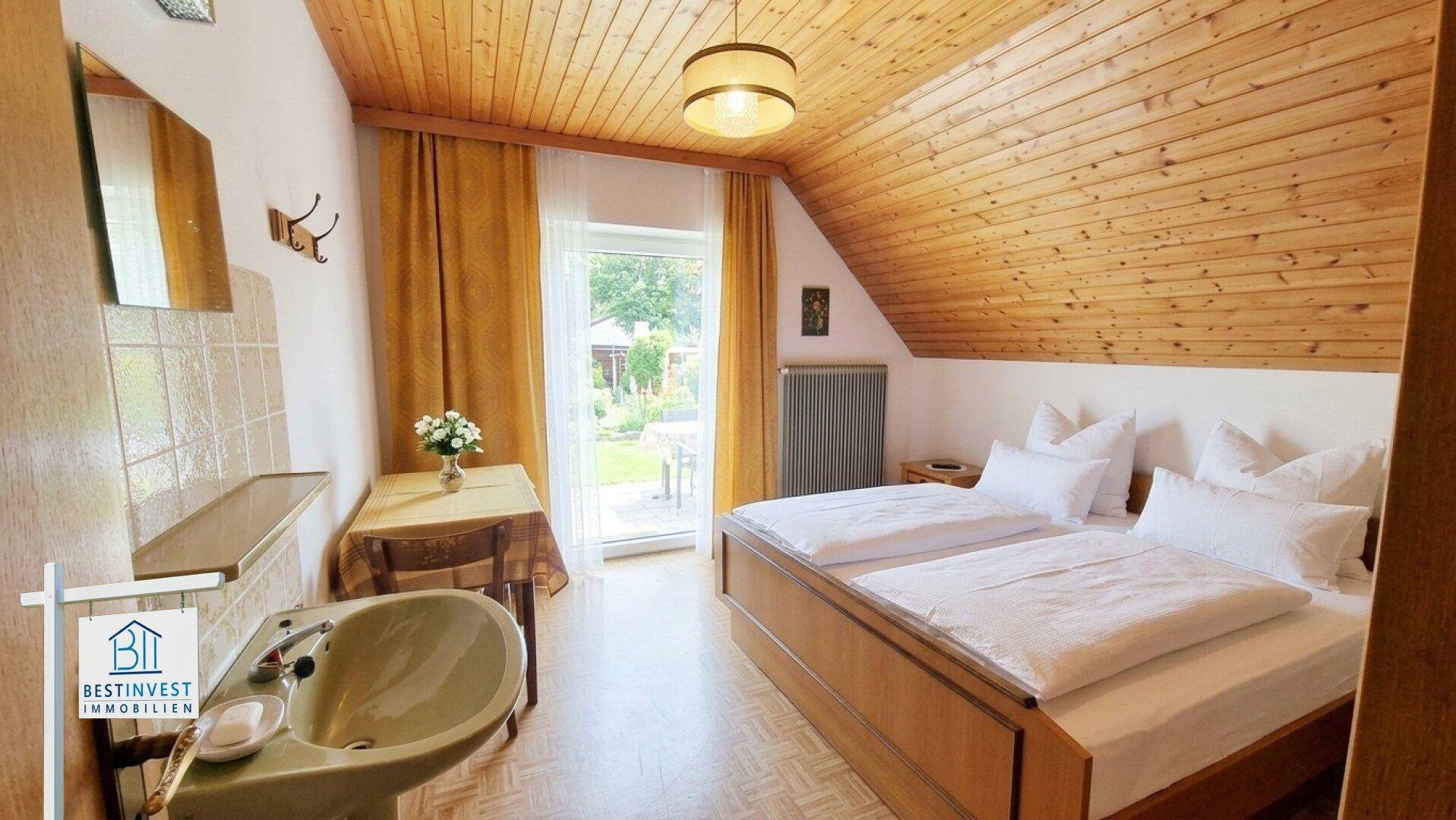 Helles Schlafzimmer mit Holzbalkendecke, Waschbecken und direktem Gartenzugang.