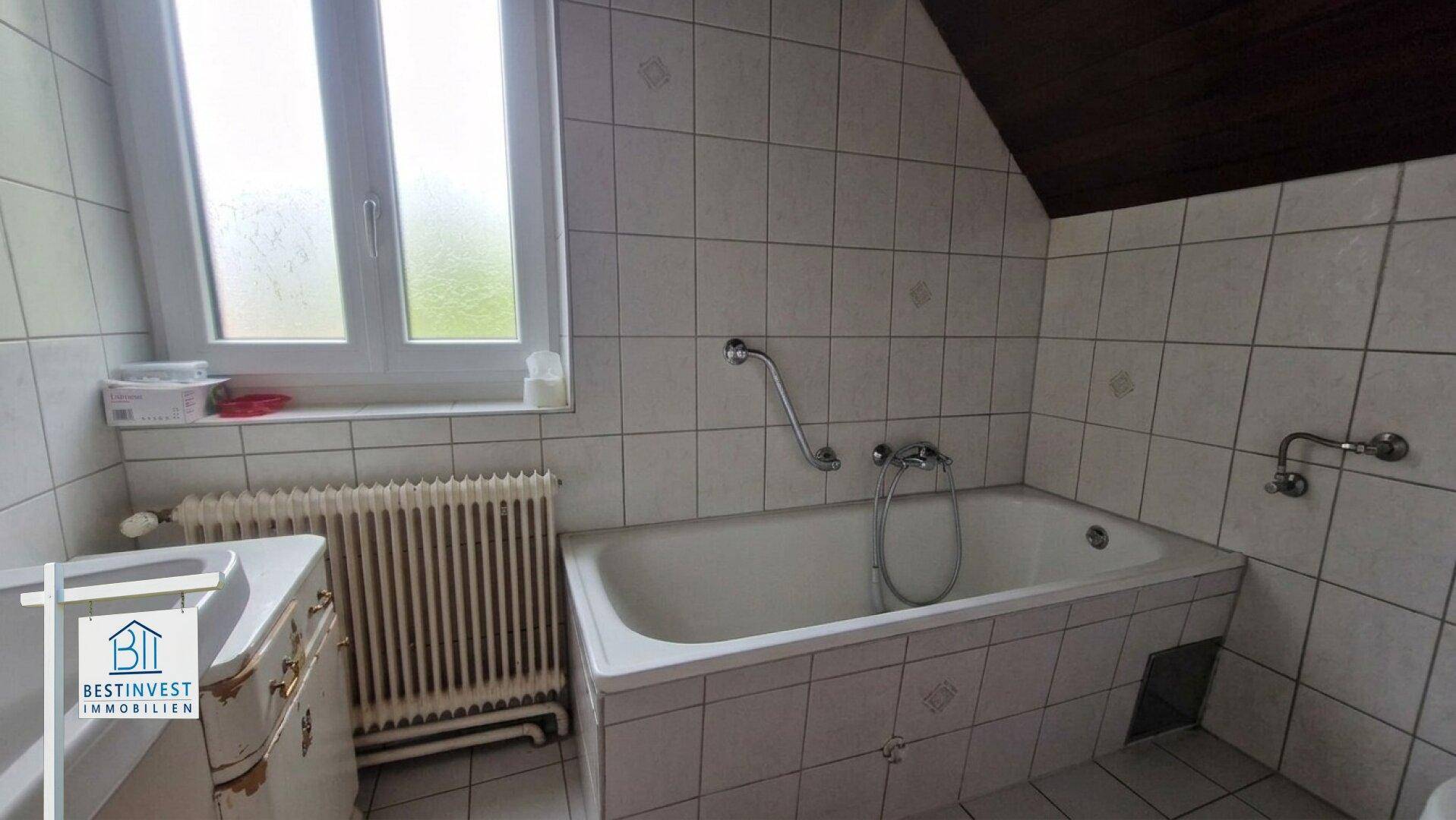 Badezimmer mit Badewanne, Fenster und weißen Fliesen, in gutem Zustand.