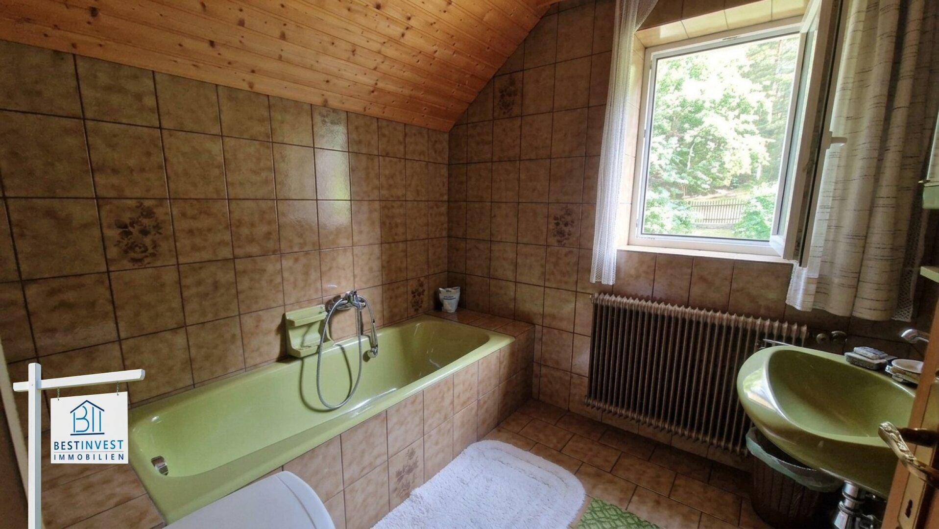 Badezimmer mit grüner Badewanne, Waschbecken und braunen Fliesen, im Dachgeschoss.