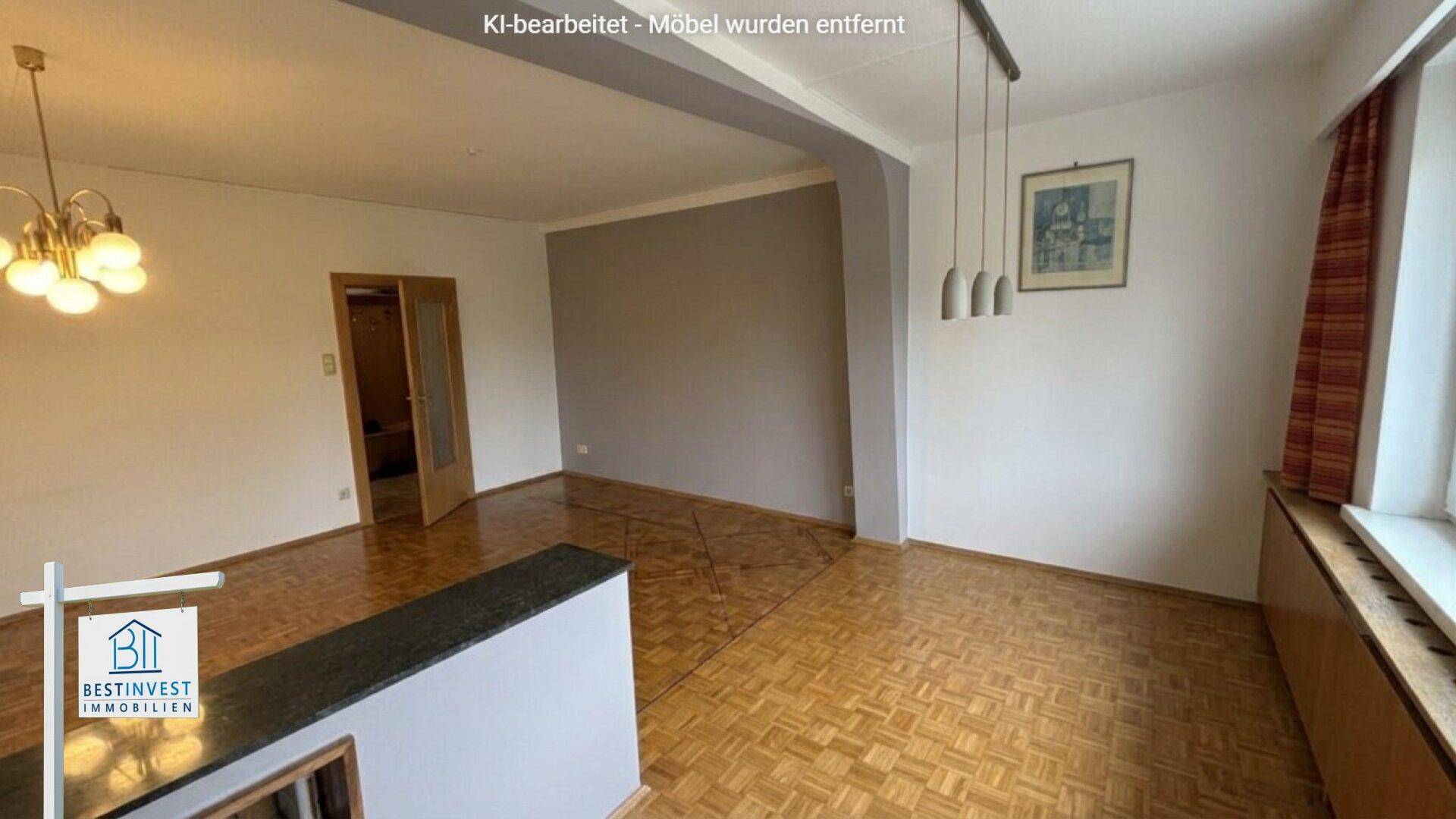 Leerer Wohnbereich mit Parkettboden, einer Trennwand und Zugang zu weiteren Räumen.