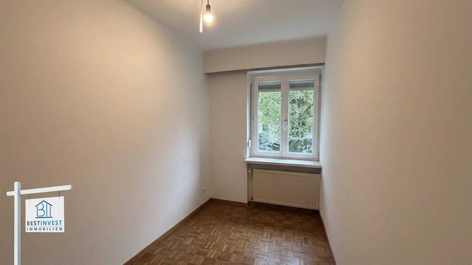 Leeres Zimmer mit Parkettboden, Fenster und Heizkörper, ideal als Schlaf- oder Arbeitszimmer.