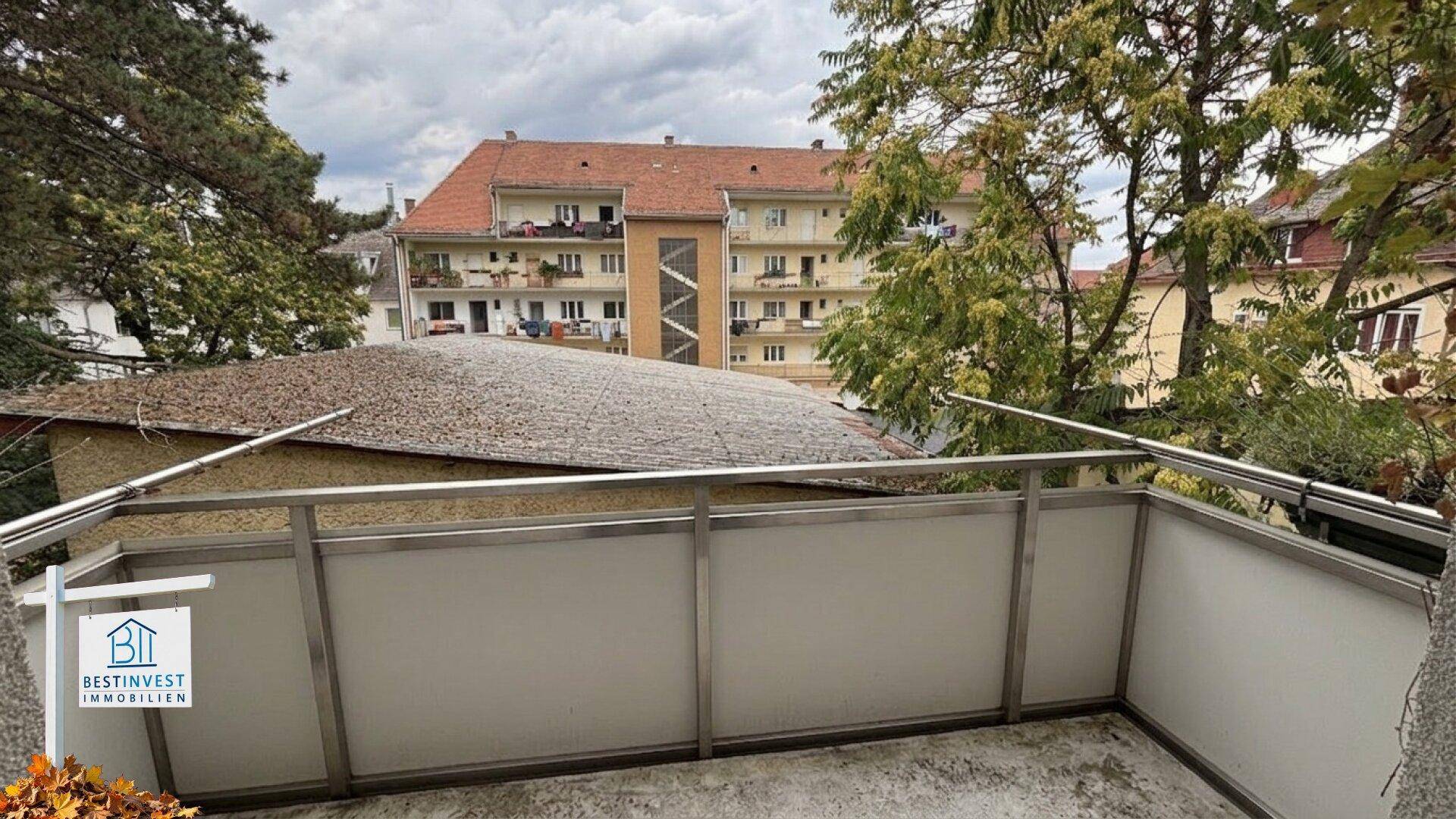 Balkon mit Metallgeländer und Blick auf umliegende Gebäude und Bäume.