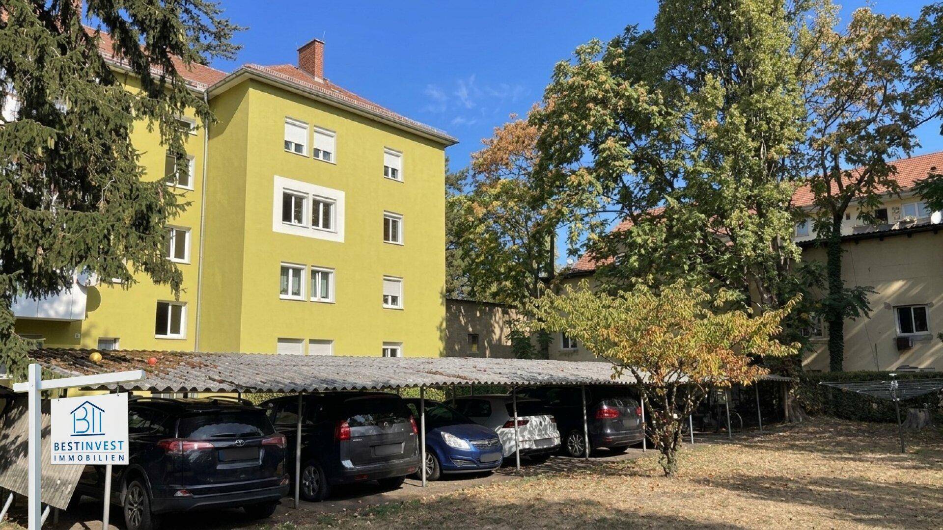 Mehrfamilienhaus mit gelber Fassade und überdachten Parkplätzen im Außenbereich.