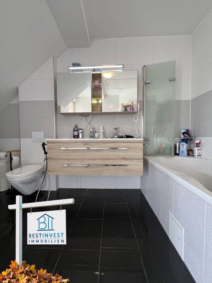 Modernes Badezimmer mit Badewanne, Doppelwaschbecken und Dachschräge, hell gefliest.