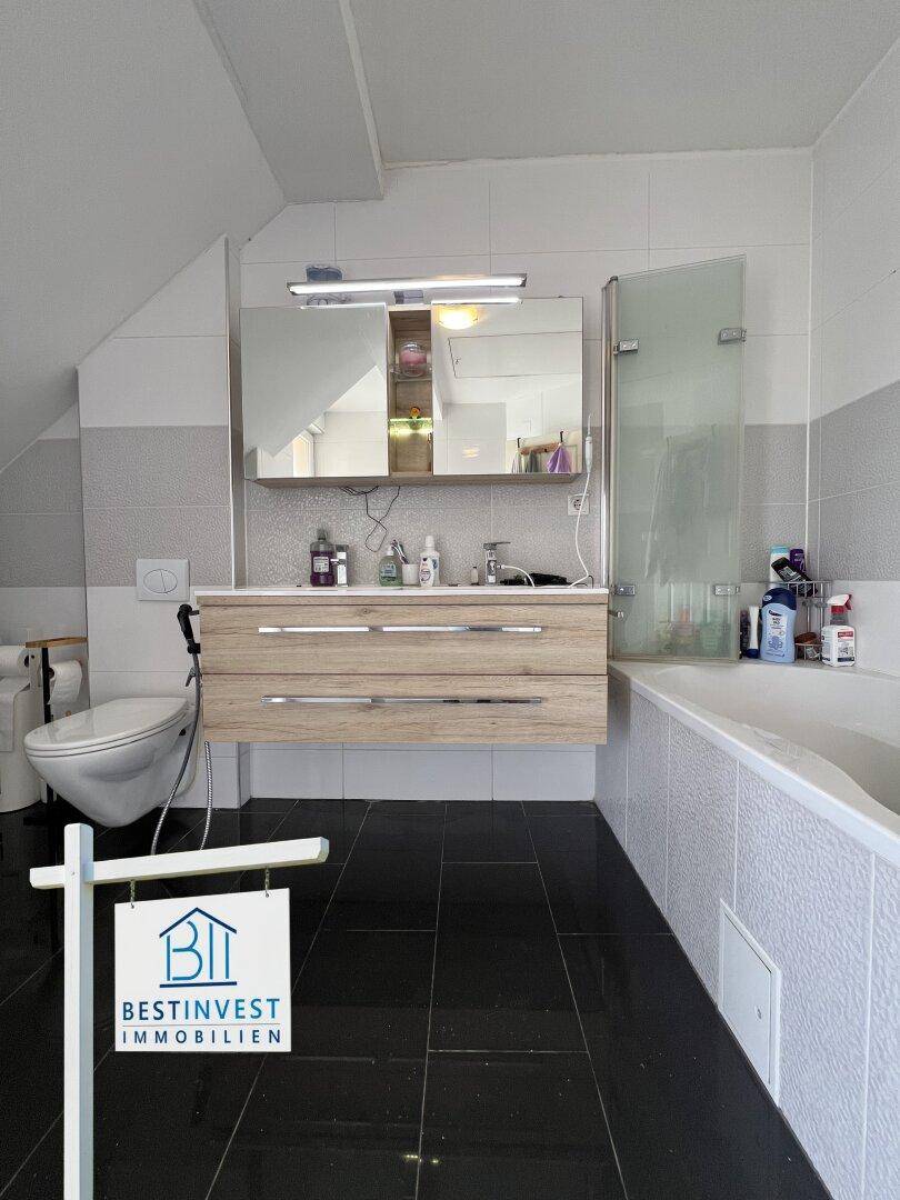 Modernes Badezimmer mit Badewanne, Waschtisch und Spiegelschrank unter der Dachschräge.