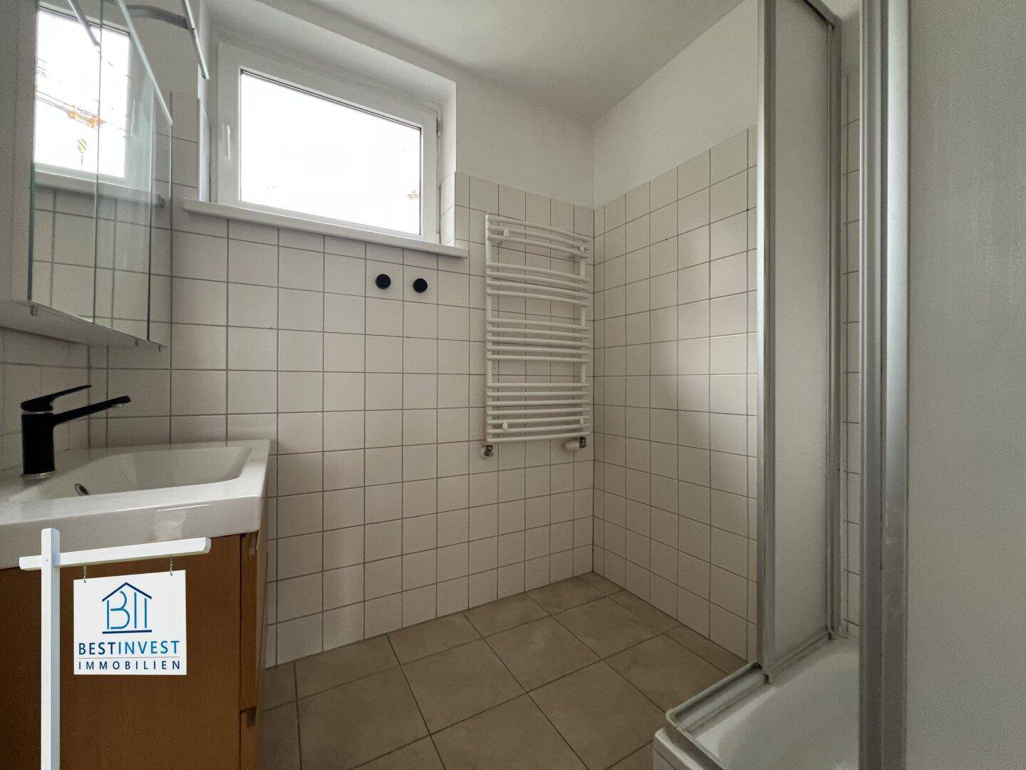 Badezimmer mit Duschkabine, Waschbeckenunterschrank, Handtuchheizkörper und Fenster.