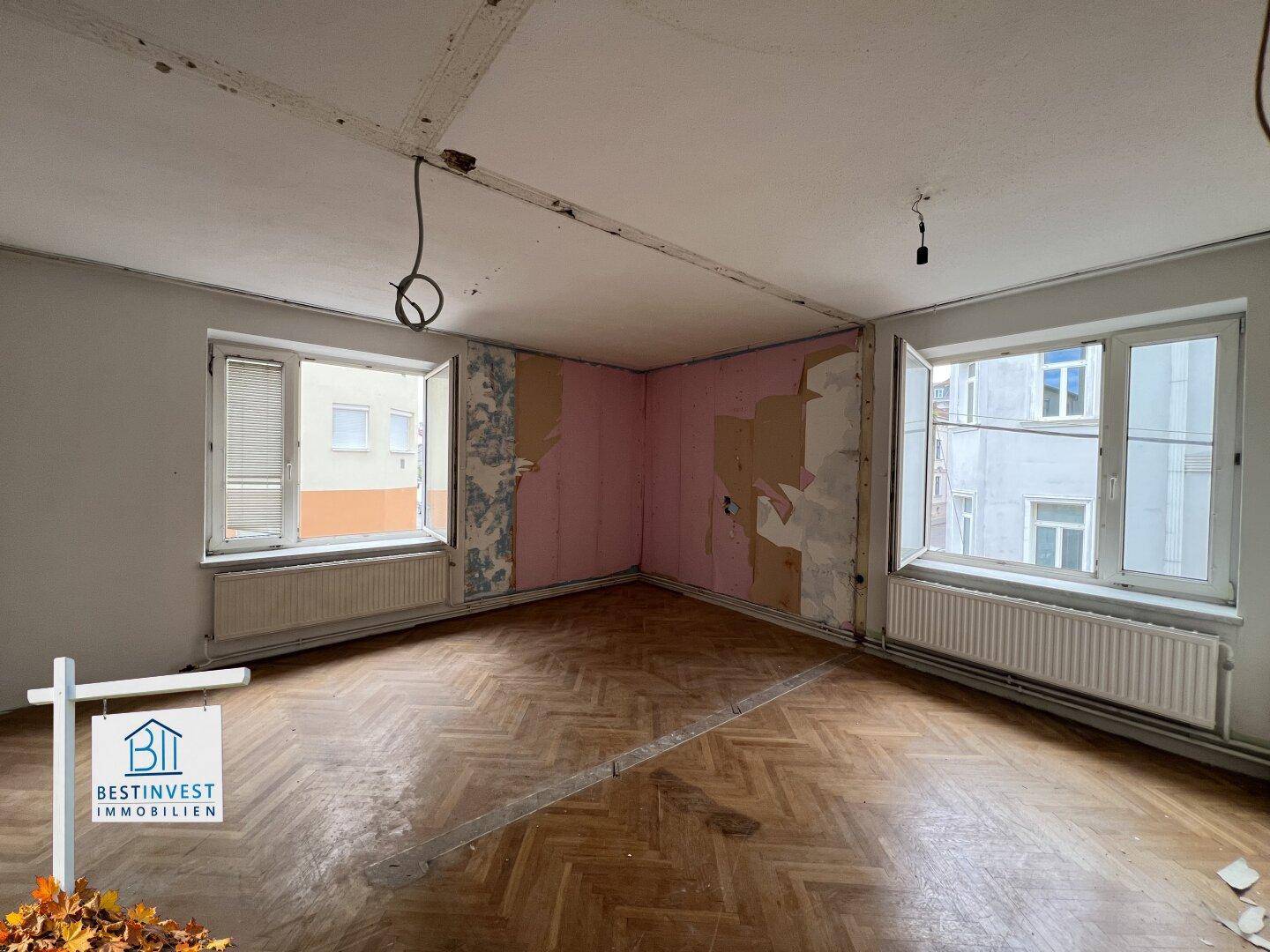 Renovierungsbedürftiges Zimmer mit Parkettboden und abgelöster Tapete, bereit für Modernisierung.