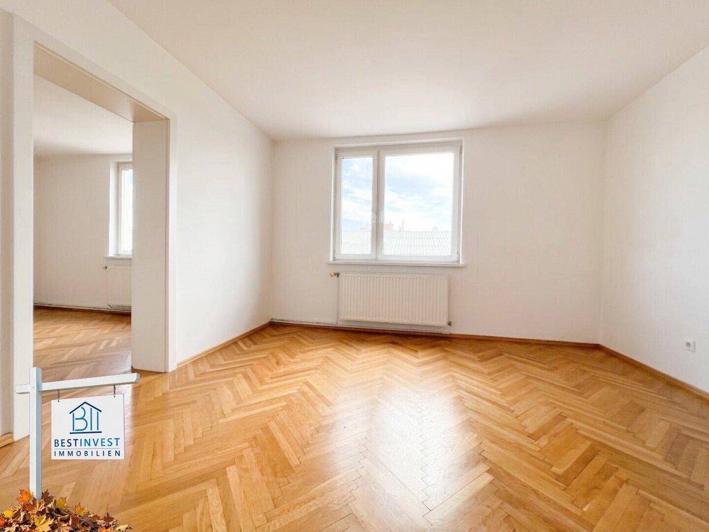 Geräumiges Zimmer mit Fischgrätparkett und großem Fenster, das viel Tageslicht hereinlässt.
