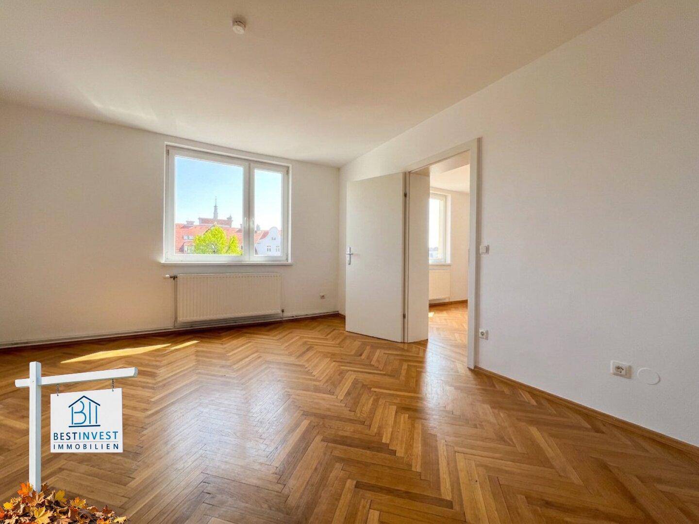 Helles Zimmer mit klassischem Fischgrätparkett und Blick auf die Stadt durch das Fenster.