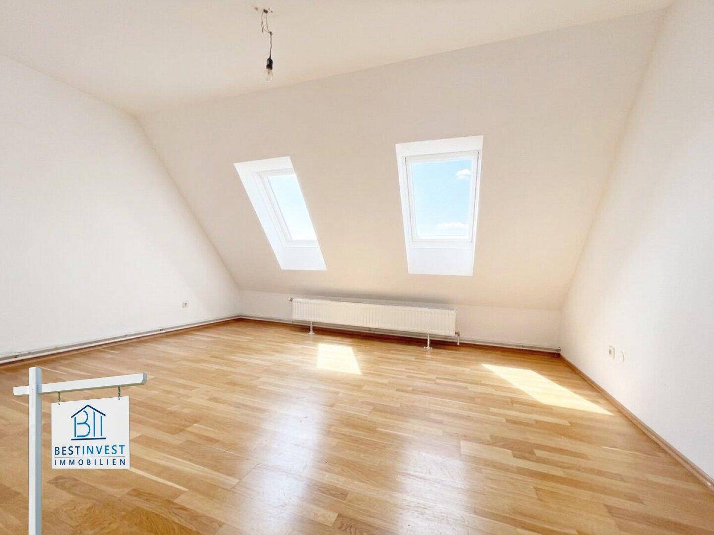 Dachgeschosszimmer mit schrägen Wänden, Holzboden und zwei Dachfenstern für viel Tageslicht.