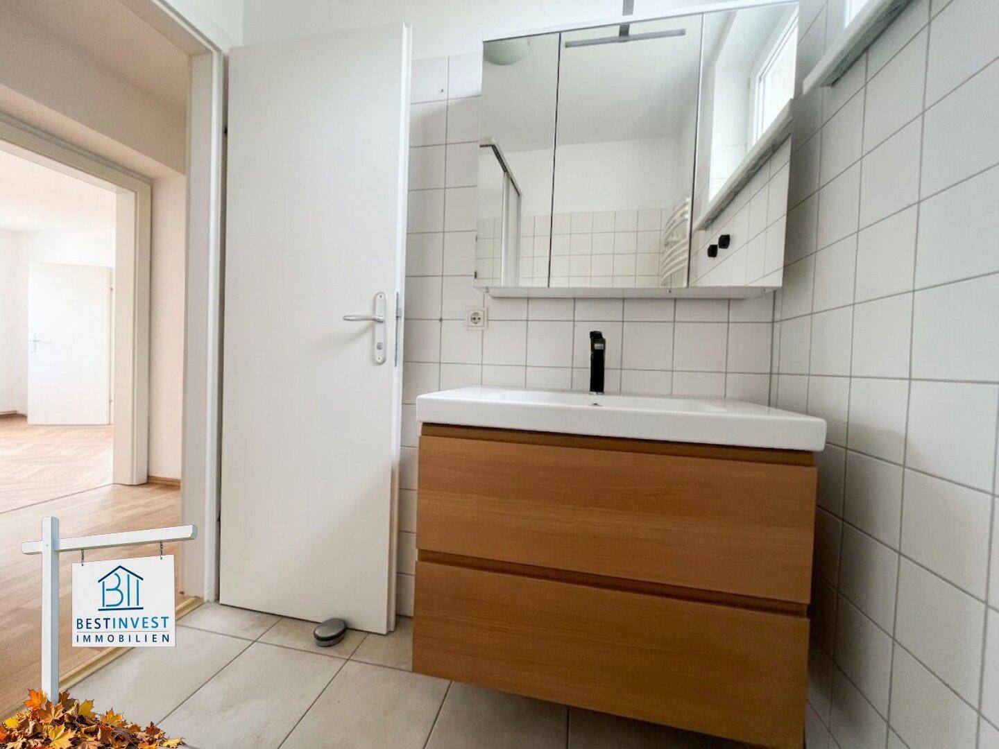 Badezimmer mit modernem Waschtisch, Spiegelschrank und weißen Fliesen, gut beleuchtet.