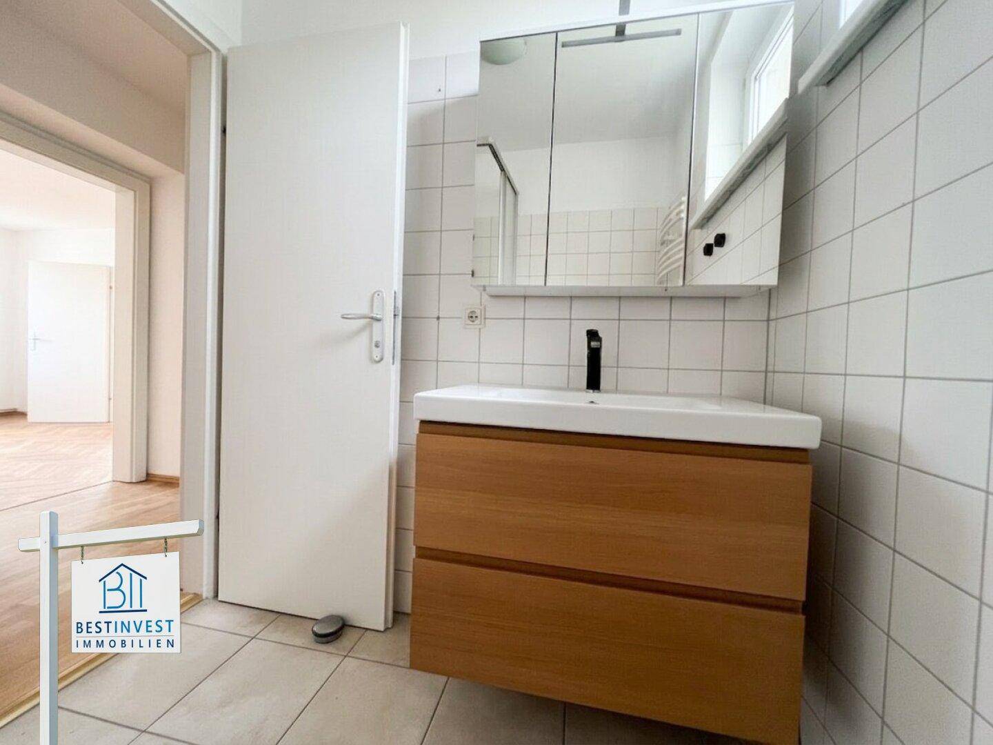 Helles Badezimmer mit modernem Waschbecken, Holzunterschrank und Spiegelschrank.