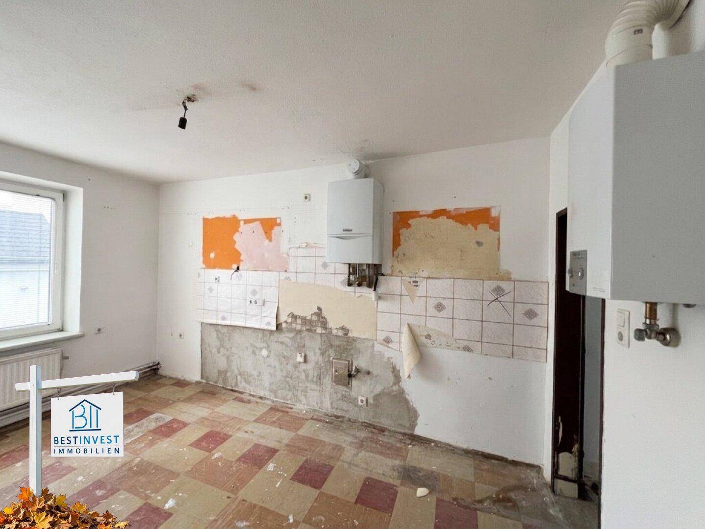 Renovierungsbedürftige Küche mit alten Fliesenresten und sichtbaren Installationen, bereit für Umbau.