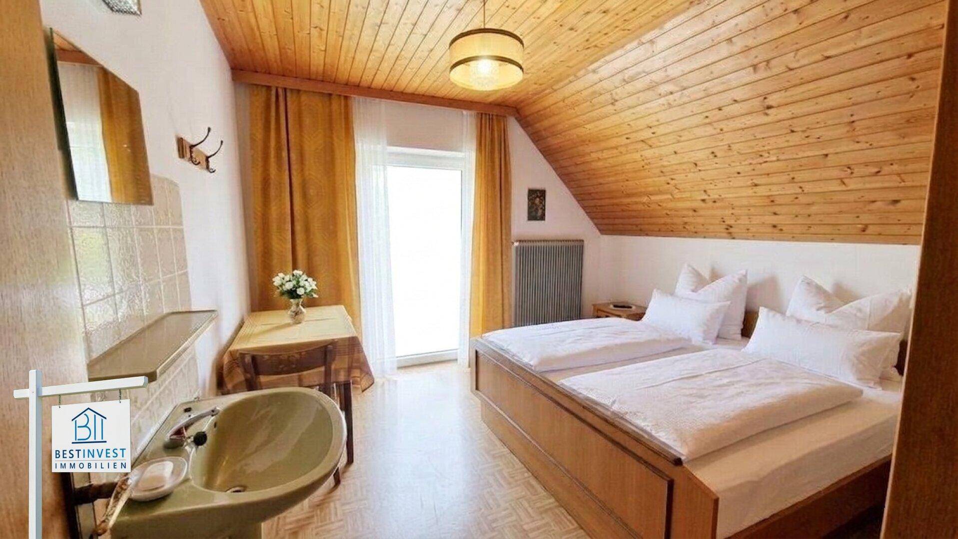 Gemütliches Schlafzimmer im Dachgeschoss mit Holzdachschräge, zwei Einzelbetten und einem Waschbeckenbereich.