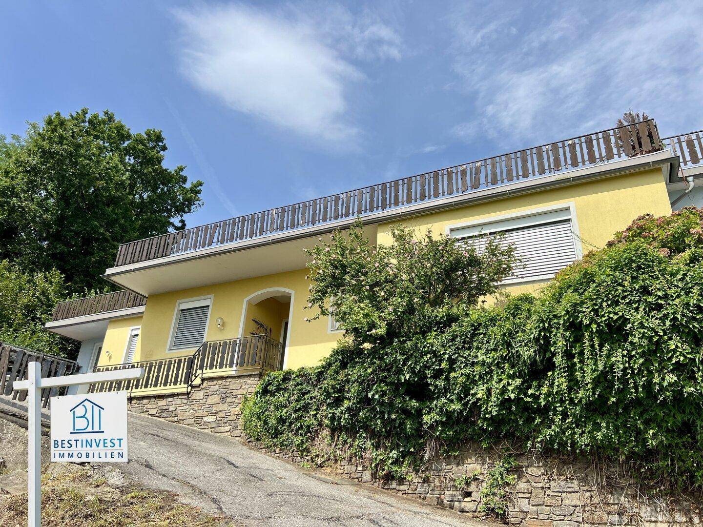 Gelbe Hausfassade mit üppiger Bepflanzung und einem Balkon im oberen Stockwerk.
