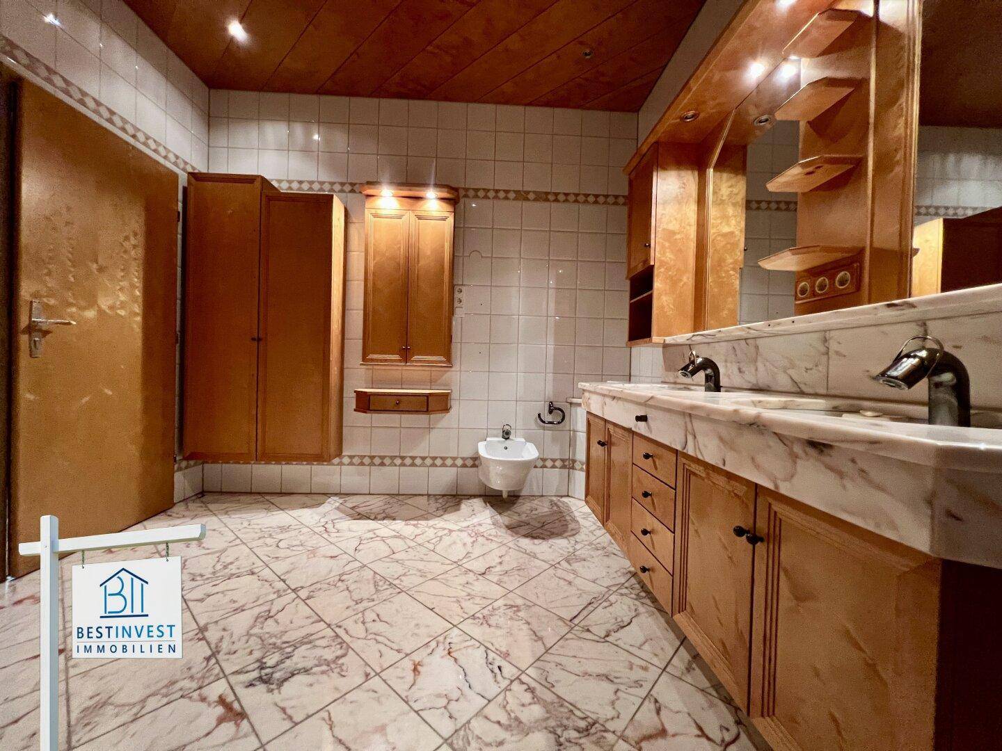 Geräumiges Badezimmer mit Doppelwaschbecken, Bidet, Marmorfliesen und Holzdecke im traditionellen Stil.